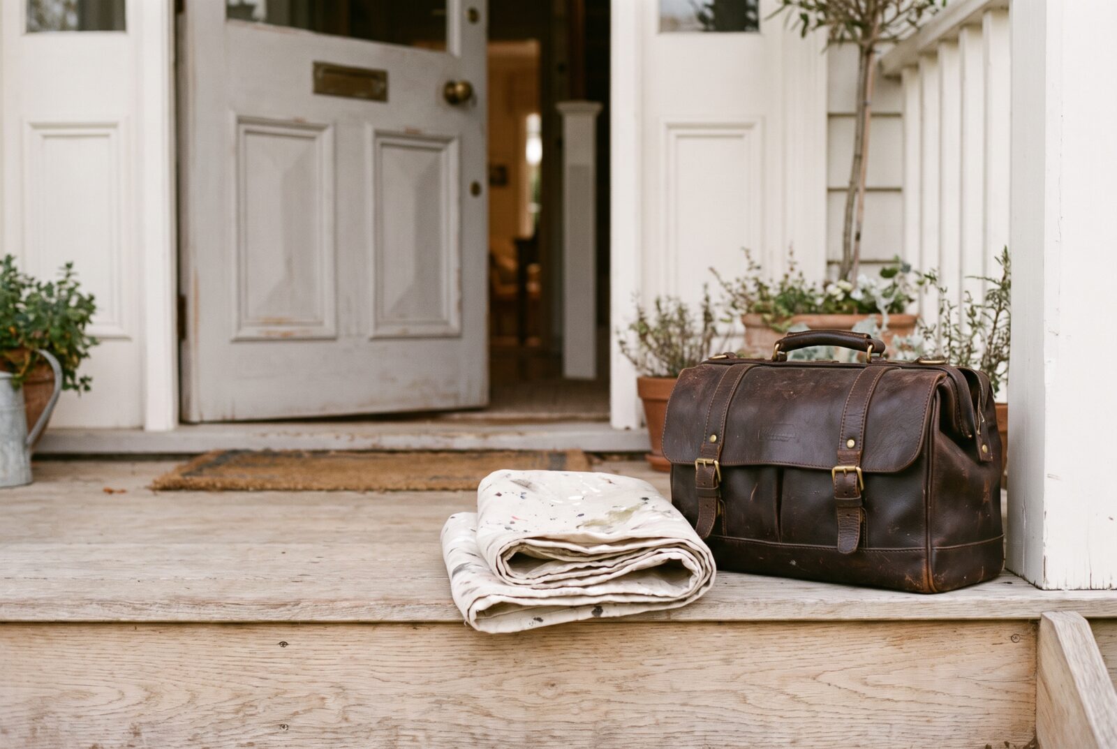A leather tool bag and folded drop cloth on the front step of a home